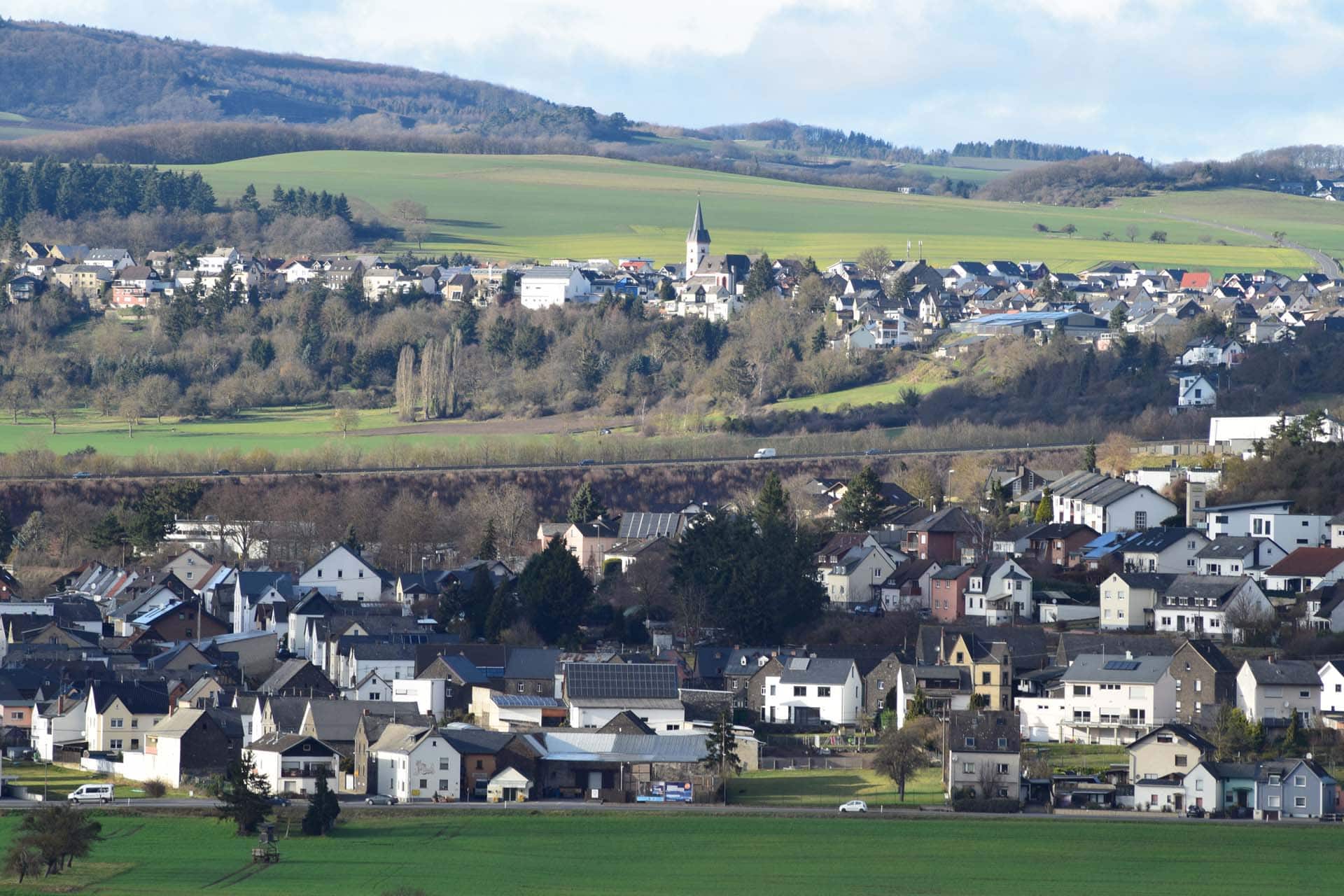 iStock-1205269656 Panoramablick auf ein Dorf in einer hügeligen Landschaft mit Kirche und grünen Feldern
