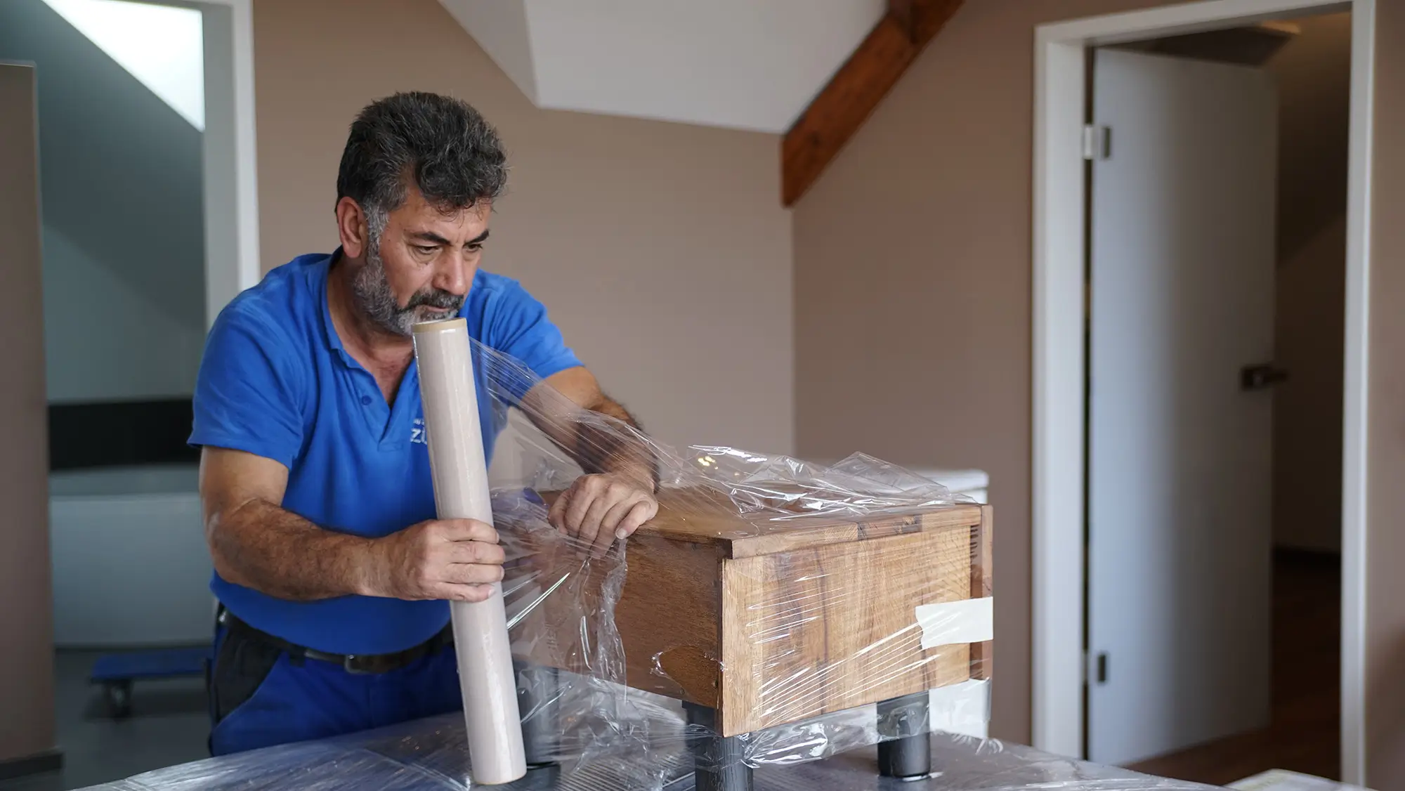 Umzugshelfer verpackt ein Holzmöbelstück sorgfältig in Schutzfolie