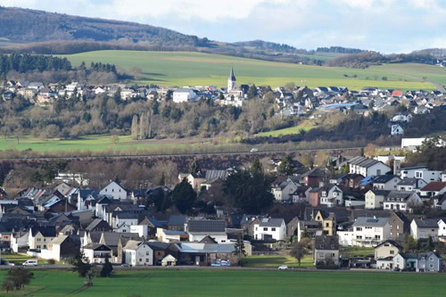 Panoramablick auf ein Dorf in einer hügeligen Landschaft mit Kirche und grünen Feldern