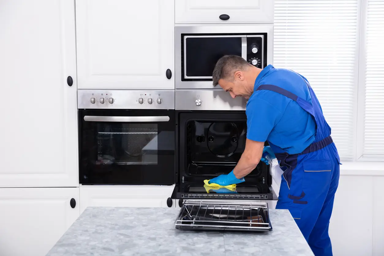iStock-1096969784 Mann in blauer Uniform führt professionelle Umzugsreinigung in einer modernen weißen Küche durch.