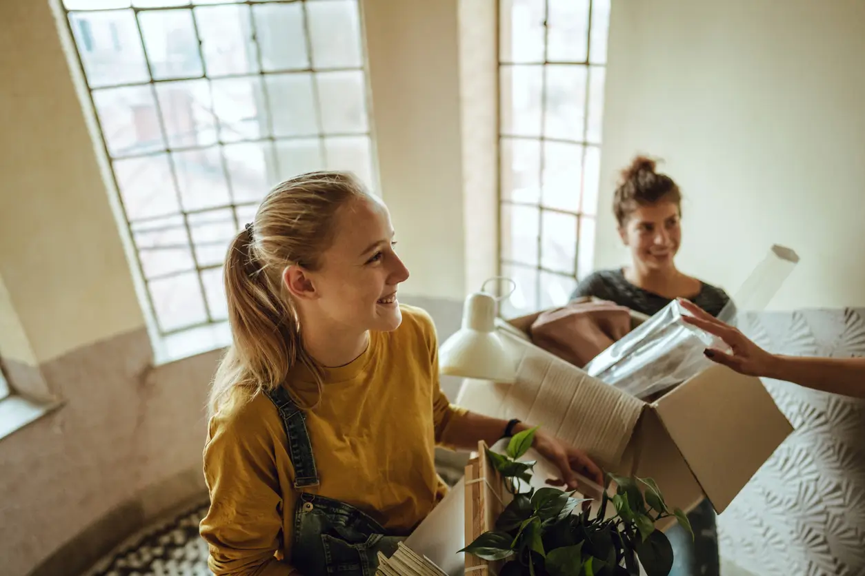 iStock-1196667100 Zwei junge Frauen lächeln beim Einzug in ihre erste eigene Wohnung, Checkliste in der Hand.