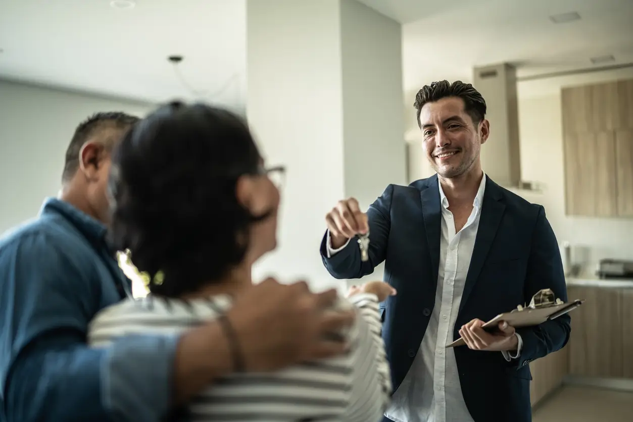 iStock-1435664395 Ein lächelnder Makler übergibt einem Paar die Schlüssel eines modernen Hauses.