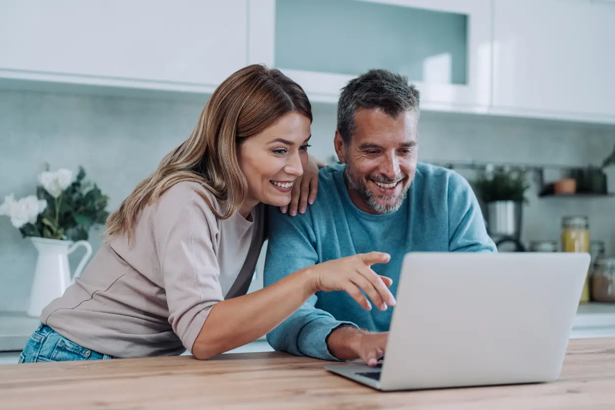 iStock-2148308279 Lächelndes Paar schaut gemeinsam in einer hellen Küche auf einen Laptop.